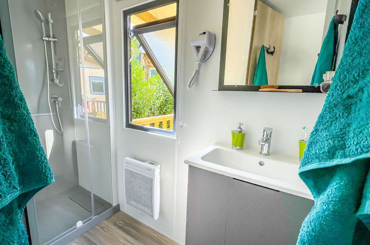 Salle de bain moderne avec grande douche, radiateur ou chauffe-serviette, et s&egrave;che-cheveux dans les cottages et lodges Premium du camping Domaine de Mesqueau.