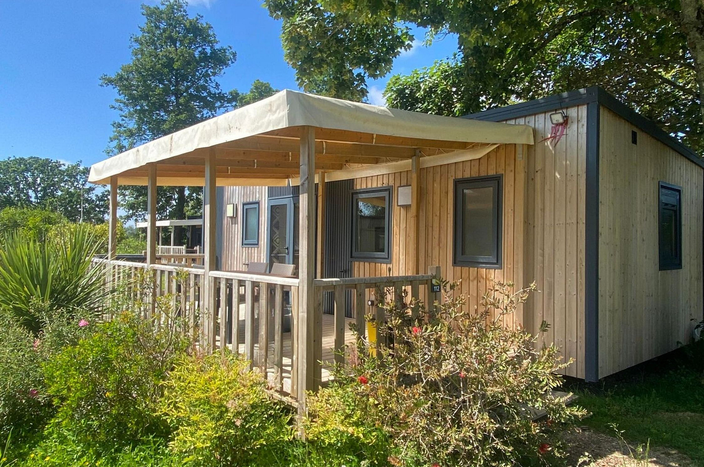 Cottage Premium 2 chambres avec bardage bois et terrasse couverte dans un environnement verdoyant au camping Domaine de Mesqueau.