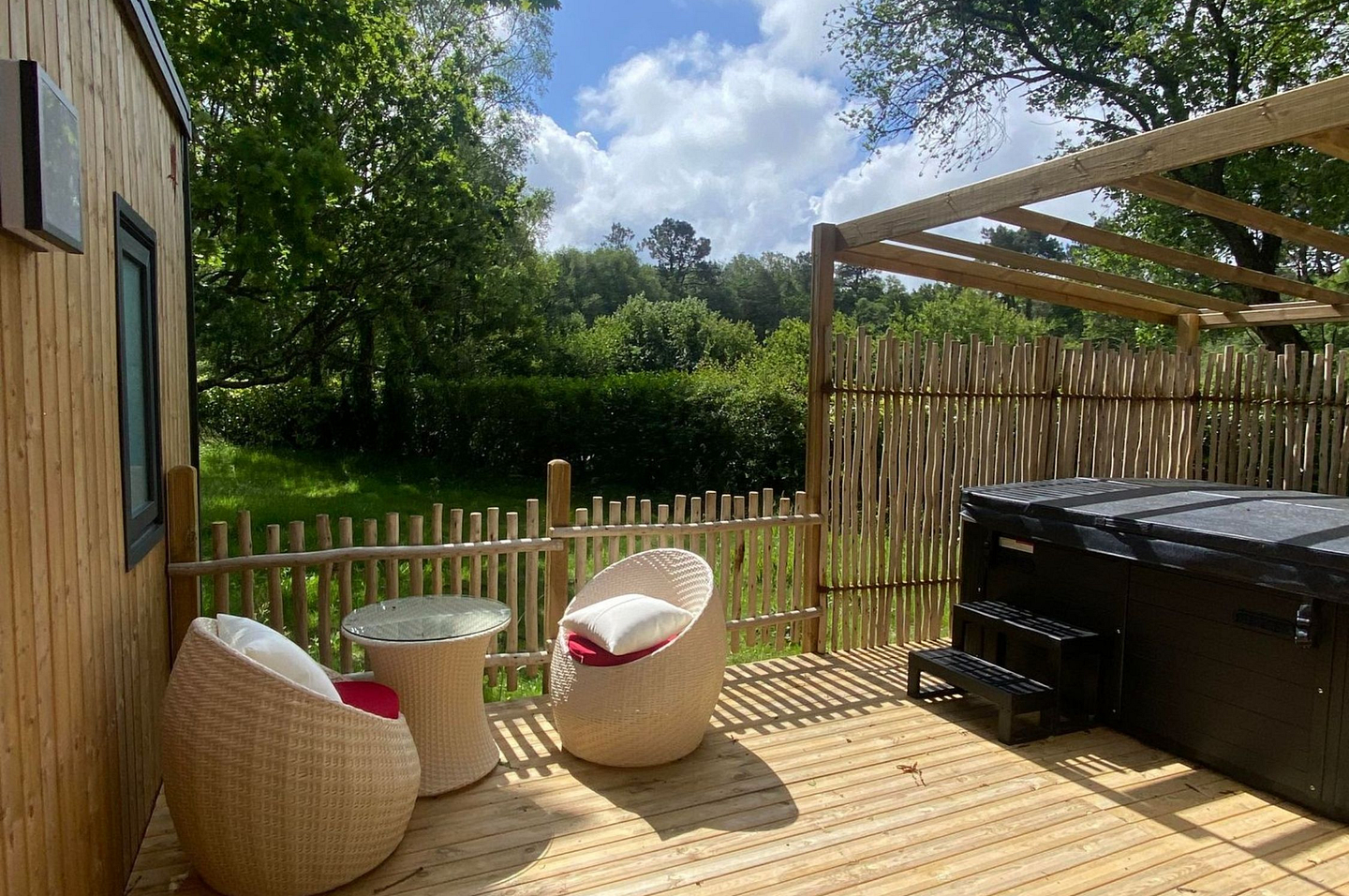 Terrasse en bois du Lodge Serenity Premium avec spa privatif et mobilier de jardin, entour&eacute;e de verdure au camping Domaine de Mesqueau.