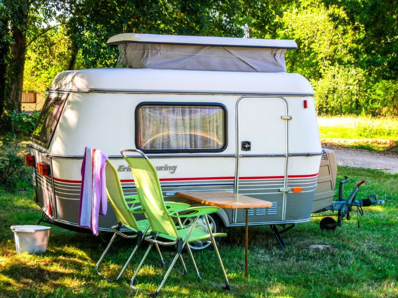 Caravane vintage install&eacute;e sur un emplacement ombrag&eacute; au camping Mesqueau avec chaises vertes et table en plein air