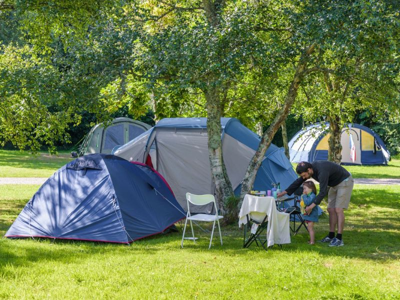 Famille install&eacute;e sur un emplacement tente ombrag&eacute; au camping Mesqueau avec jeune enfant et table de pique-nique