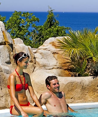 Camping Le Bois de Valmarie - Parc aquatique - Couple se relaxant dans la piscine avec la mer Méditerranée en fond