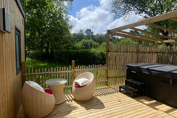 Terrasse en bois du Lodge Serenity Premium avec spa privatif et mobilier de jardin, entour&eacute;e de verdure au camping Domaine de Mesqueau.