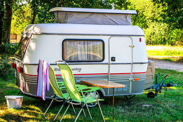 Caravane vintage install&eacute;e sur un emplacement ombrag&eacute; au camping Mesqueau avec chaises vertes et table en plein air
