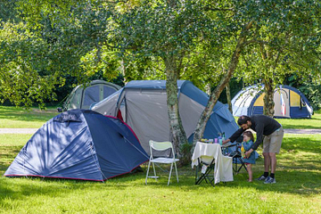 Famille install&eacute;e sur un emplacement tente ombrag&eacute; au camping Mesqueau avec jeune enfant et table de pique-nique
