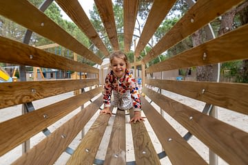 Camping Les Couleurs de la Coubre - Activités et animations - Enfant dans un tunnel en bois de l\'aire de jeux