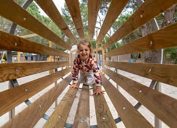 Camping Les Couleurs de la Coubre - Activités et animations - Enfant dans un tunnel en bois de l\'aire de jeux