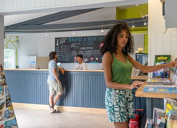 Camping Le Logis - Receptie - Paar arriveert bij de receptie - Man praat met de receptioniste en vrouw raadpleegt toeristische informatie