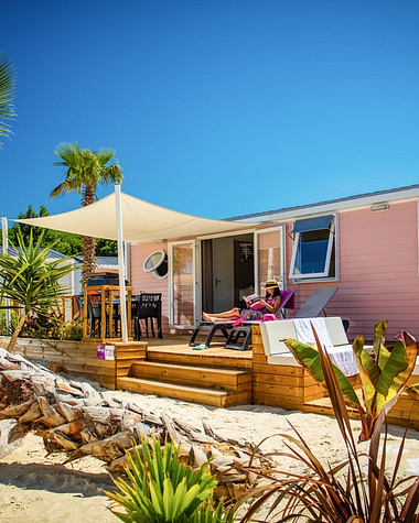 Camping Californie Plage - Locations - Hébergement avec terrasse semi couverte entouré de palmiers