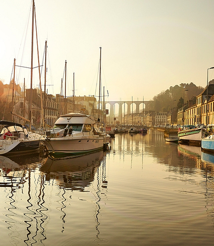 Vue sur le port de Morlaix avec des voiliers et le viaduc illumin&eacute; par la lumi&egrave;re du lever de soleil.
