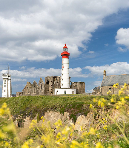 Phare de Saint-Mathieu et ruines historiques entour&eacute;es de fleurs sauvages, avec un ciel bleu et des nuages en arri&egrave;re-plan en Bretagne.