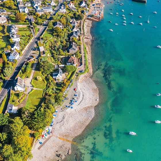 Vue a&eacute;rienne d&rsquo;un village c&ocirc;tier breton avec plage de galets, maisons typiques et bateaux ancr&eacute;s, en Bretagne