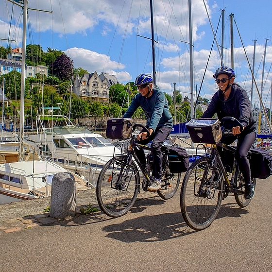 Couple à vélo longeant le port de Morlaix, en Bretagne, par une journée ensoleillée.