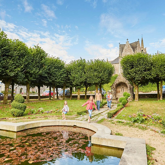 Famille se promenant dans le parc de Guerlesquin avec église historique en arrière-plan, jardin bien entretenu et étang, Bretagne