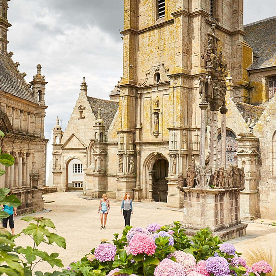 Visiteurs explorant le clo&icirc;tre de Saint-Th&eacute;gonnec, c&eacute;l&egrave;bre pour ses sculptures d&eacute;taill&eacute;es et son architecture historique en Bretagne.