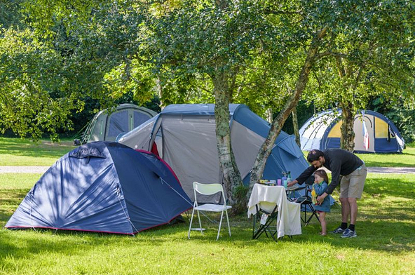 Famille installée sur un emplacement tente ombragé au camping Mesqueau avec jeune enfant et table de pique-nique