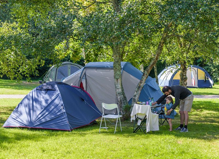 Famille install&eacute;e sur un emplacement tente ombrag&eacute; au camping Mesqueau avec jeune enfant et table de pique-nique